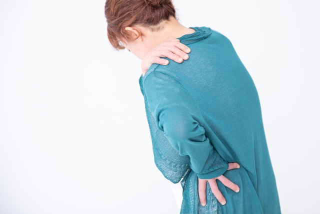 肩の痛みで首から肩に手をあてる女性の後ろ姿