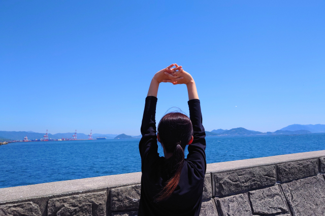 海辺で伸びをする女性の後ろ姿