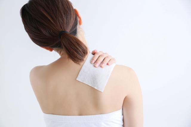 肩に湿布を貼る女性の後ろ姿