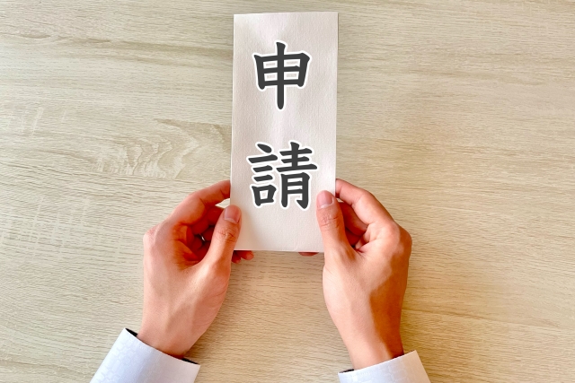 「申請」と書かれた紙を持つ手