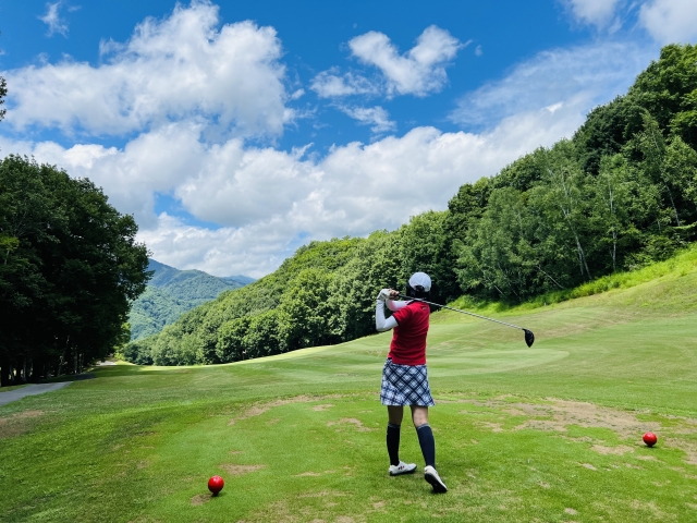 山を背にティーショットを打つ女性ゴルファー