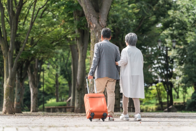 スーツケースを引いて歩く高齢の夫婦の後ろ姿