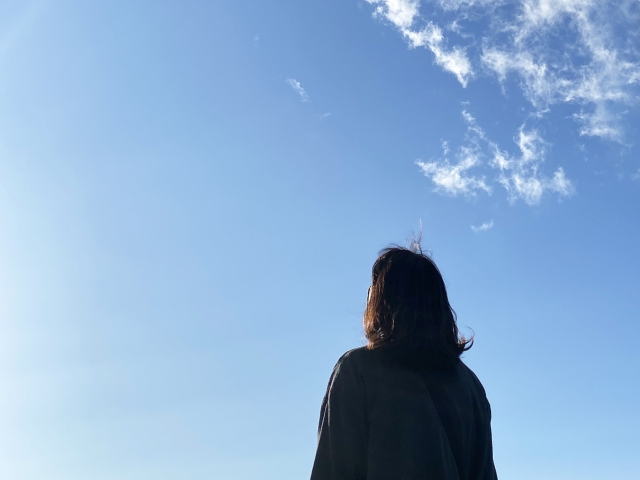 青空を見上げる女性の後ろ姿