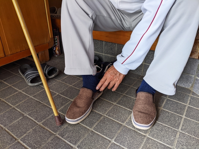 玄関に立てかけられた杖と、靴を履く足元